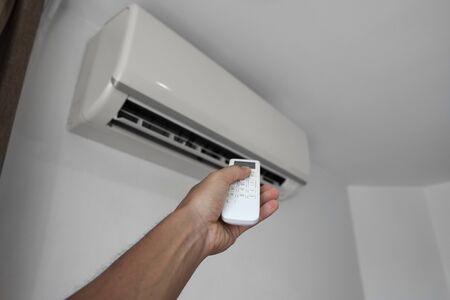 Mans hand using remote controler. Hand holding rc and adjusting temperature of air conditioner mounted on a white wall. Indooor comfort temperature. Health concepts and energy savings.の写真素材