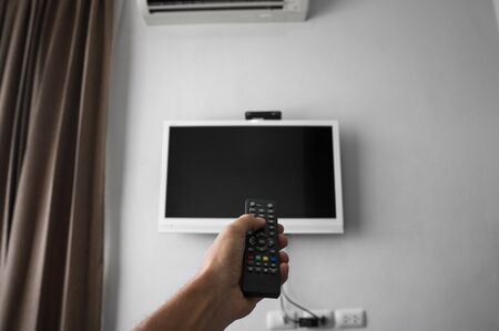 The man with the remote control in hand want switch on the TV and presses the button on the remote control. Remote control in hand closeup.の写真素材