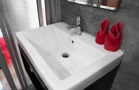 Modern stainless steel faucet with wash basin sink with a two red towels on it . Counter bathroom interior contemporary. Luxury and stylish design bathroom with a concrete style walls.の写真素材