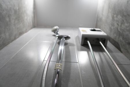 Instant tankless electric water heater installed on grey tile wall with input and output pipe/outlet and elcb safety breaker system and silver shower.の写真素材