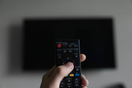 The man with the remote control in hand want switch on the TV and presses the button on the remote...