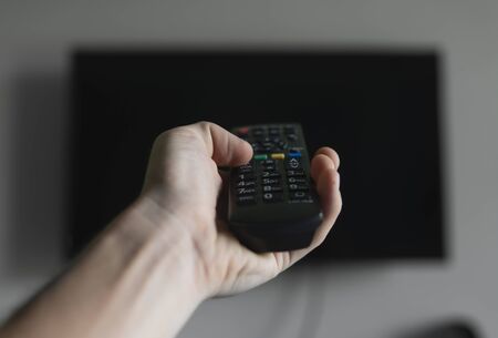 The man with the remote control in hand want switch on the TV and presses the button on the remote control. Remote control in hand closeup.の写真素材