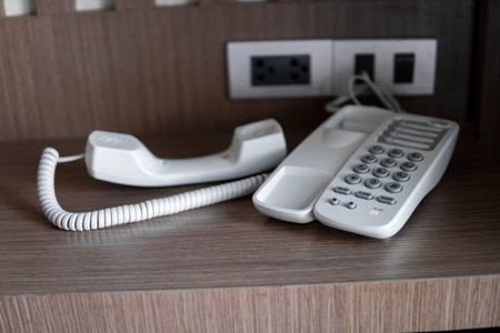 Remove headset of white vintage telephone with grey buttons on a brown table in hotel.
