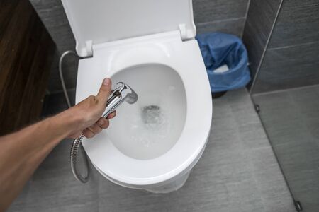 Using of bidet shower with a white toilet. Bidet shower in male hand for using with a white toilet bowl.の写真素材