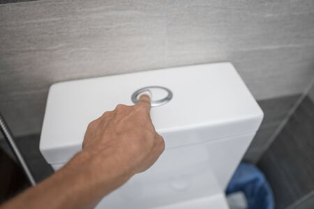 Close up of finger pushing a flush toilet button for cleaning a toilet.の写真素材