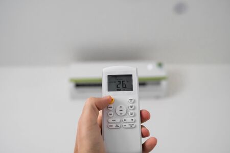 Mans hand using remote controler. Hand holding rc and adjusting temperature of air conditioner mounted on a white wall. Indooor comfort temperature. Health concepts and energy savings.の写真素材