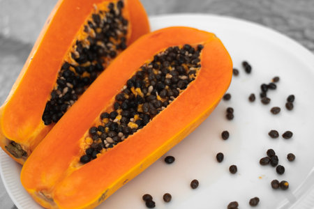 Half cut ripe papaya with seed on a white plate. Slices of sweet papaya with a white background....