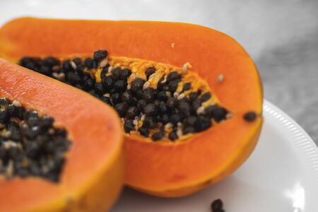 Half cut ripe papaya with seed on a white plate. Slices of sweet papaya with a white background. Halved papayas. Healthy exotic fruits. Vegetarian foodの写真素材