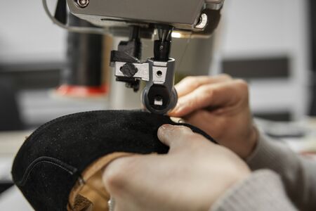 Sewing machine in a leather workshop in action with hands working on a leather details for shoes. Women's hands with sewing machine at shoes factoryの写真素材