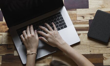 Womans hands typing on laptop keyboard top view. Study and work online, freelance. Self employed or freelance woman, girl working with her laptop sitting at wooden table with a phone and ereader.の写真素材