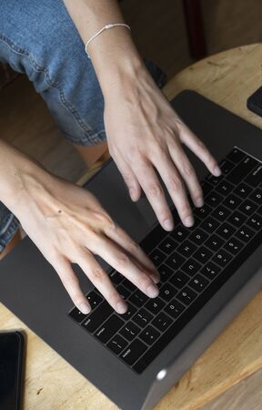 Woman is sitting on a sofa and using a laptop at wooden table. Study and work online, freelance. Self employed girl is working with her notebook sitting on a couch with a phone and ereader on table.の写真素材