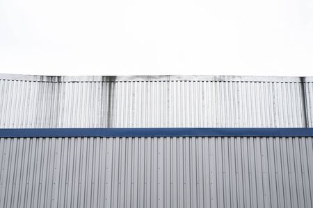 Metal corrugated sheets on a building with a blue metal corners. White aluminium metal corrugated roof or wall sheets against cloudy sky background on a factories and industrial buildings.の写真素材