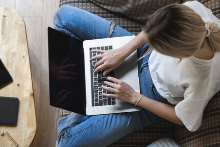 Woman with a laptop sitting on a sofa. Study and work online, freelance. Self employed woman, girl working with her notebook sitting on a couch with a phone, smartphone and ereader on table.の写真素材