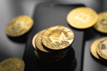 Stack of golden Monero bitcoin coin on a smartphone with a lot of bitcoins coins on a table. Virtual...