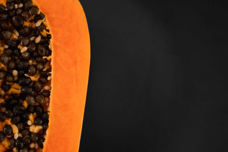 Half of ripe papaya with seed on a black plates and with a green plants on background. Slices of...