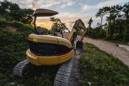 The modern excavator on the construction site with sunset sky. Large tracked excavator standing on a hill with a green grass. Machinery for a construction of a new building in the countryside.の写真素材