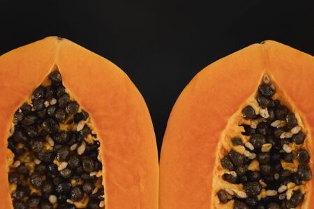 Half of ripe papaya with seed on a black plates and with a green plants on background. Slices of sweet papaya. Halved papayas. Healthy exotic fruits. Vegetarian foodの写真素材