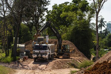 THAILAND, PHUKET - December 12, 2018: Using an excavator to translate large pipes into a vehicle helping a person.のeditorial素材