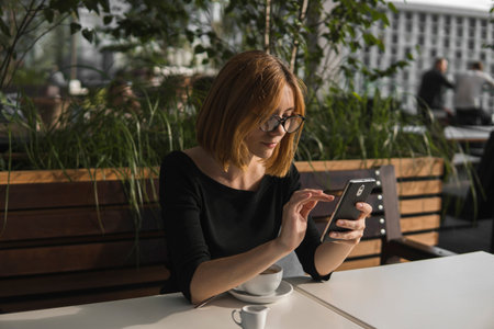 Young business woman uses phone. Good looking brunette female uses online banking on smart phone to...