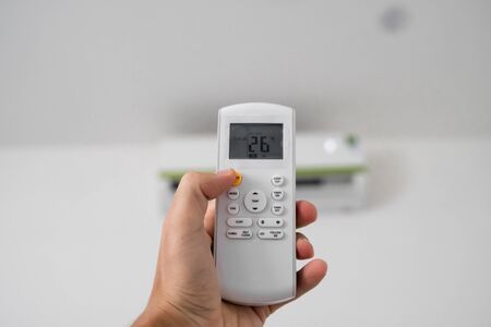 Mans hand using remote controler. Hand holding rc and adjusting temperature of air conditioner mounted on a white wall. Indooor comfort temperature. Health concepts and energy savings.の写真素材