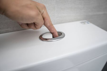 Close up of finger pushing a flush toilet button for cleaning a toiletの写真素材