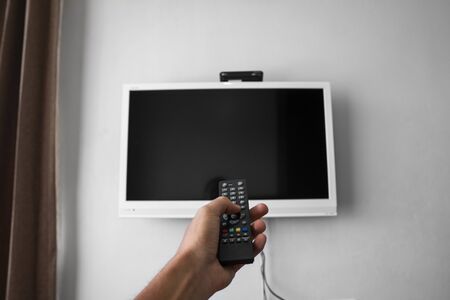 The man with the remote control in hand want switch on the TV and presses the button on the remote control. Remote control in hand closeupの写真素材