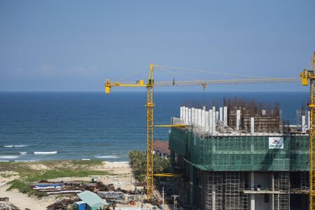 VIETNAM, DA NANG - April 10, 2019: Cranes and building construction site against blue sky and sea. Metal construction of unfinished building on construction. Tower Crane use for building of multi storage building.のeditorial素材