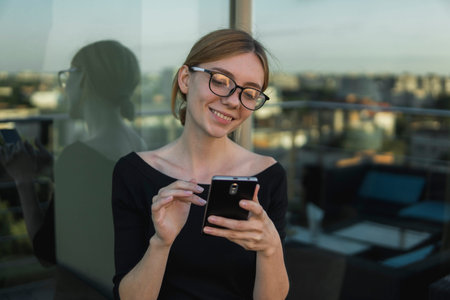 Smiling Young business woman uses phone. Good looking brunette female using smart phone and chatting with business partners and receive a good news.の写真素材