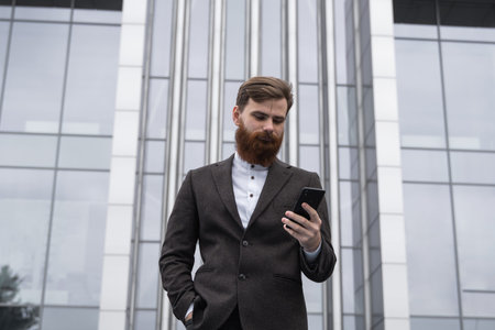 Young bearded Businessman holding mobile smartphone using app texting sms message wearing jacket...