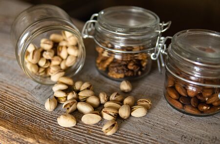 Pistachios scattered on the white vintage table from a jar and with other nuts on background. Pistachio is a healthy vegetarian protein nutritious food. Pistachios on rustic old woodの写真素材