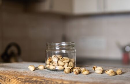 Pistachios in a jar and scattered Pistachios around a jar which standing on a white vintage table with a kitchen on background. Pistachio is a healthy vegetarian protein nutritious food.の写真素材