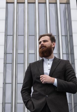 Portrait of an handsome businessman wearing jacket over office building in financial district outdoors. Young bearded Businessman outdoor. Successful entrepreneur dressed in formal wear.の写真素材