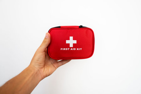 Man's hand holding a red first-aid kit with a white wall on background