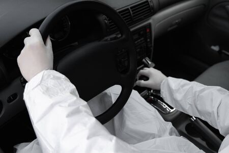 Man in protective suit, medical mask and rubber gloves for protect himself from bacteria and virus is driving car. Protective mask while quarantine, world pandemic, covid 19, coronavirus, infection.の写真素材