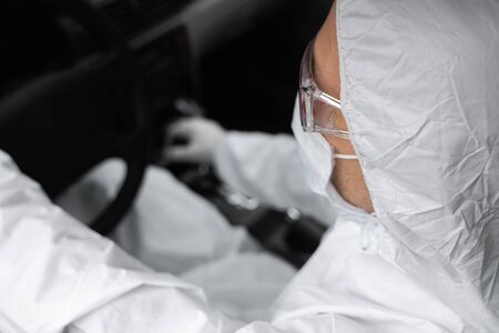 Man in protective suit, medical mask and rubber gloves for protect from bacteria and virus is driving a car. Protective mask while quarantine, world pandemic, covid 19, coronavirus, infection.の写真素材
