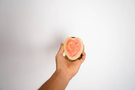 Female hand holding a half of ripe guava on a white backgroundの写真素材