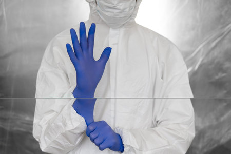 Doctor in white protective suit, mask, glasses and rubber gloves is ready for helping a people while...