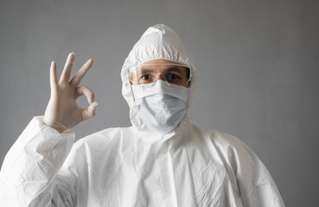 Doctor in white protective suit, medical mask and rubber gloves is showing that everything is fine....