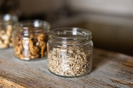 Sunflower seeds, walnut and pistachio in a jars which standing on a white vintage table with a...