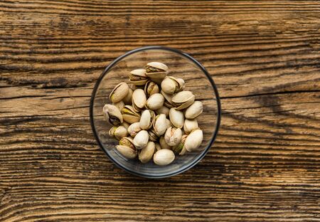 Pistachios in a small plate on a vintage wooden table as a background with a copy space. Pistachio is a healthy vegetarian protein nutritious food. Natural nuts snacks.の写真素材
