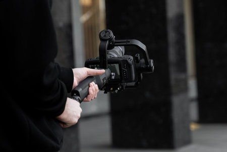 Professional videographer in black hoodie holding professional camera on 3-axis gimbal stabilizer....