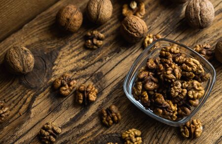 Walnut in a smale plate with scattered shelled nuts and whole nut which standing on a wooden vintage table. Walnuts is a healthy vegetarian protein nutritious food. Walnut on rustic old wood.の写真素材