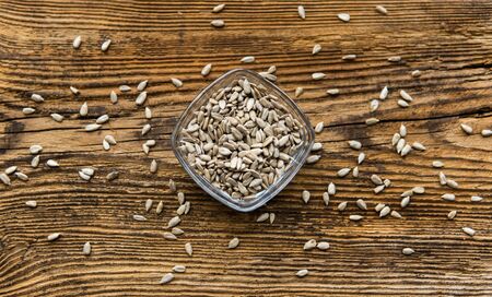 Sunflower seeds in a small plate and scattered seed on the wooden vintage table. Healthy vegetarian protein nutritious food. Sunflower seed on rustic old woodの写真素材