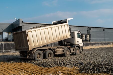 A dump truck is dumping gravel on a construction site. Dump truck dumps its load of gravel on a new road construction project. Road building. Preparing of the fundament for a asphaltingの写真素材
