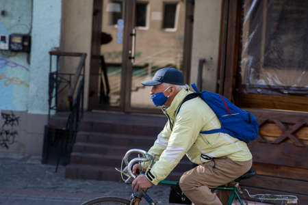 UKRAINE, KYIV - April 25, 2020: Man wearing a medical mask to prevent of bacterial infection Corona virus or Covid 19 epidemic is riding bicycle on the street.のeditorial素材