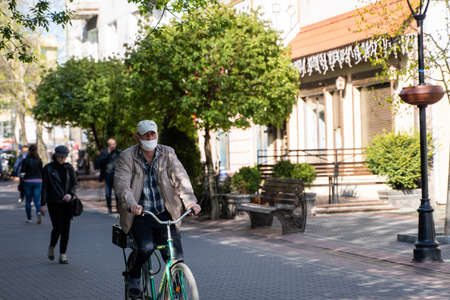 UKRAINE, KYIV - April 25, 2020: Man wearing a medical mask to prevent of bacterial infection Corona virus or Covid 19 epidemic is riding bicycle on the street.のeditorial素材
