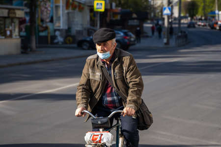 UKRAINE, KYIV - April 25, 2020: Man wearing a medical mask to prevent of bacterial infection Corona virus or Covid 19 epidemic is riding bicycle on the street.のeditorial素材