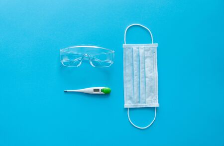 Medical protective mask, thermometer and protective glasses lie on a pink background. Anti-virus protection kit against covid-19. Coronavirus pandemic 2019.の写真素材