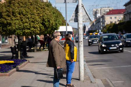 UKRAINE, KYIV - April 25, 2020: Man and Woman is stands on a the street near a traffic lights wearing a medical mask to prevent of bacterial infection Corona virus or Covid 19 epidemic on street.のeditorial素材