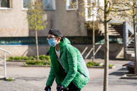 UKRAINE, KYIV - April 25, 2020: Boy rides a bmx on a street wearing a medical mask to prevent of bacterial infection Corona virus or Covid 19 epidemic on street.のeditorial素材